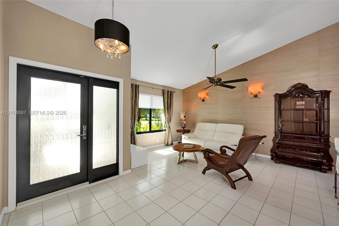 Vaulted ceilings, textured wall treatment, ceramic tile flooring, modern pendant chandelier, and glass-paneled entry door