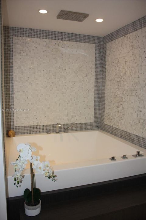 Drop-in soaking tub featuring a deck-mounted faucet and hand shower, encased in custom millwork with mosaic tile wall surrounds and recessed ceiling lighting