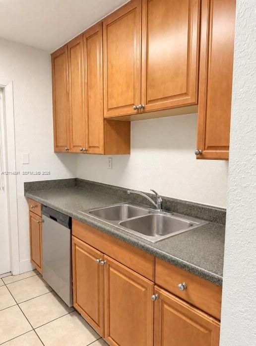 Kitchen featuring wood cabinetry, stainless steel dishwasher, double-basin stainless steel sink, and tile flooring