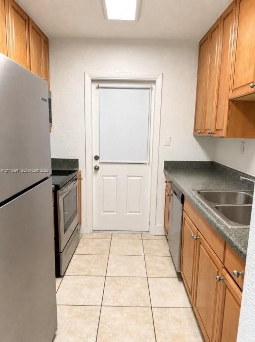 Kitchen featuring wood cabinetry, stone-finish countertops, stainless steel appliances, double-basin sink, and tile flooring