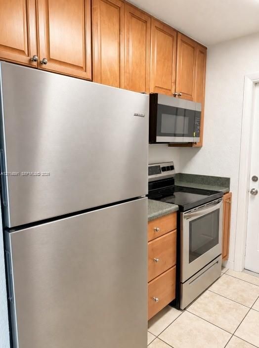 Kitchen featuring stainless steel refrigerator, built-in microwave, range, wood-finish cabinetry, and tile flooring