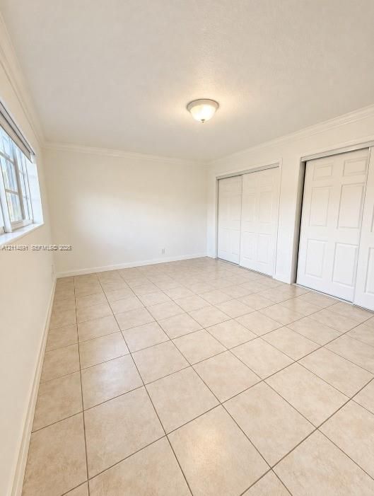 Room featuring neutral tile flooring, crown molding, multi-pane window, and dual sliding-panel closets with six-panel doors
