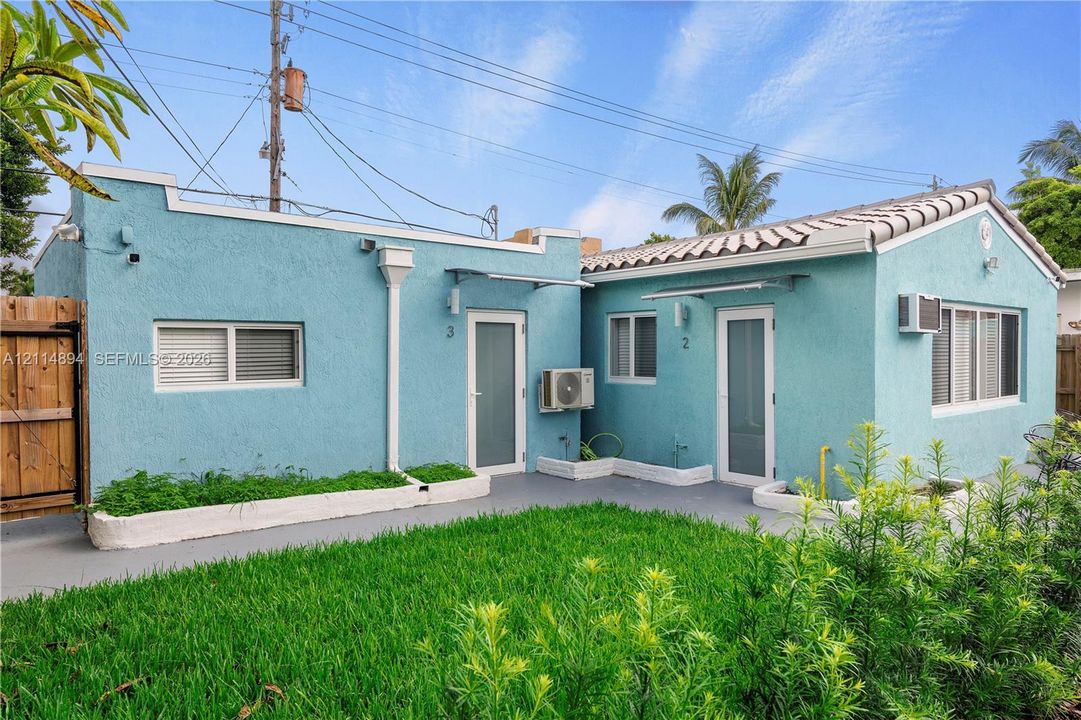 Stucco exterior featuring dual entryways, tile roof accents, and a grass courtyard with perimeter planting beds