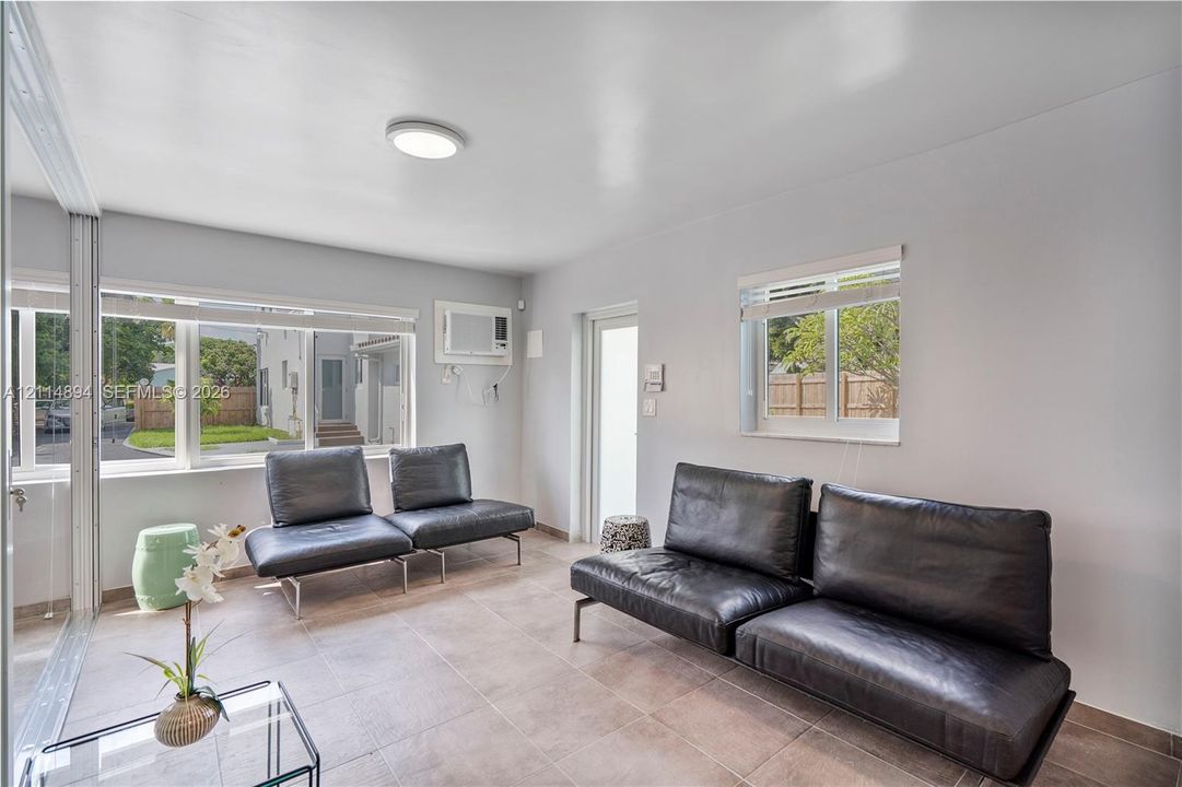 Neutral-toned room featuring large windows, stone-tile flooring, flush-mount lighting, and a wall-mounted air conditioning unit