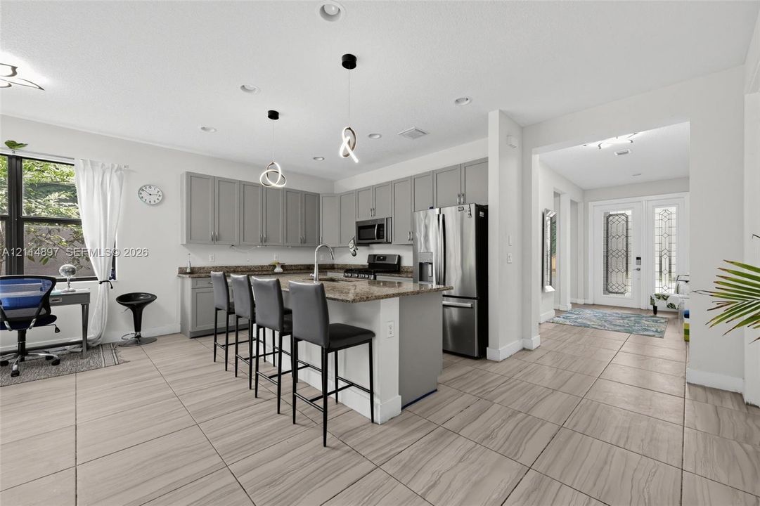 Kitchen featuring grey cabinetry, stone countertops, stainless steel appliances, tiled flooring, and modern pendant lighting