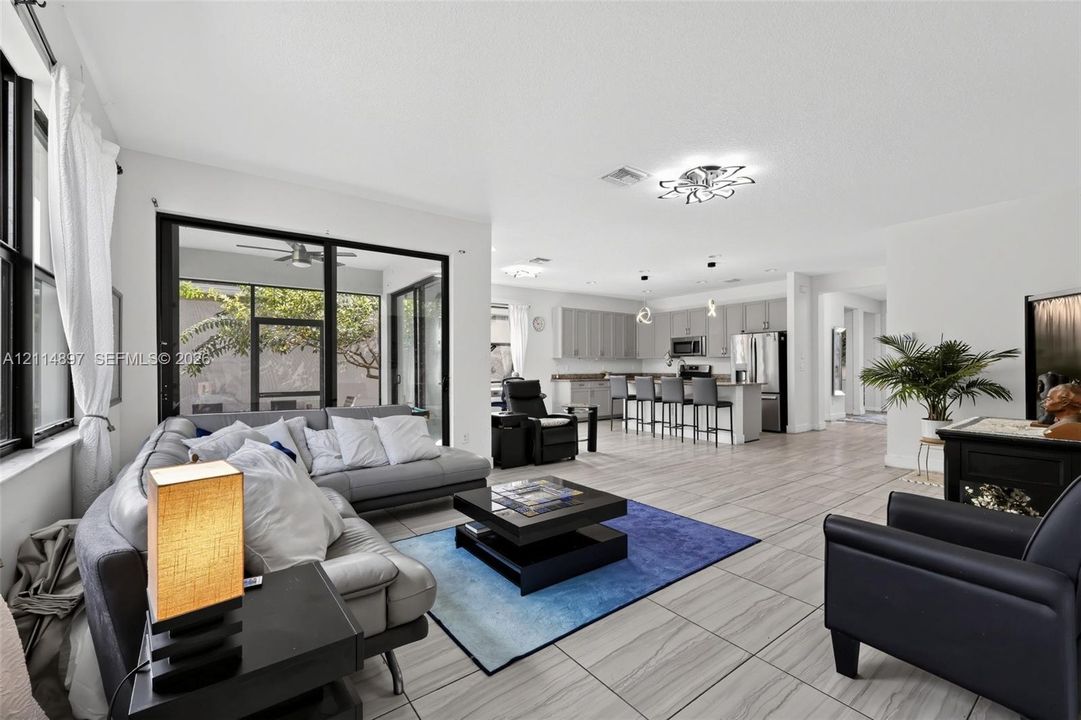Open-concept interior featuring large-format tile flooring, recessed lighting, decorative ceiling fixtures, and expansive glass sliding doors leading to a screened-in enclosure