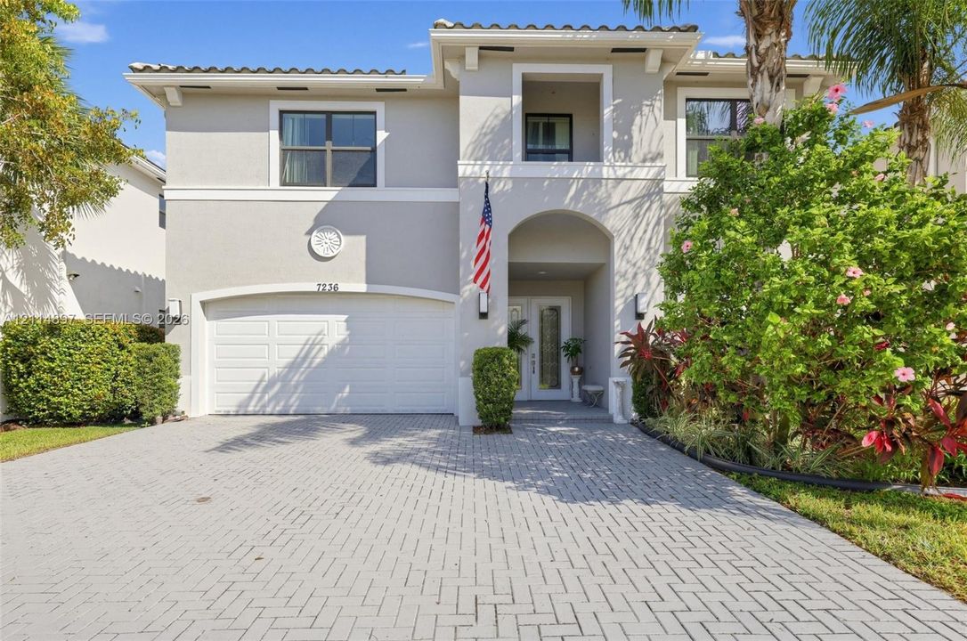 Two-story stucco exterior featuring a barrel tile roof, arched entryway, double-door glass entry, and paver driveway