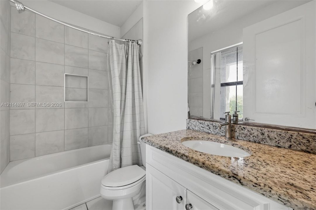 Bathroom featuring a stone-topped vanity with an integrated basin, white cabinetry, a tub-shower combination with floor-to-ceiling tile surround, and a built-in recessed wall niche