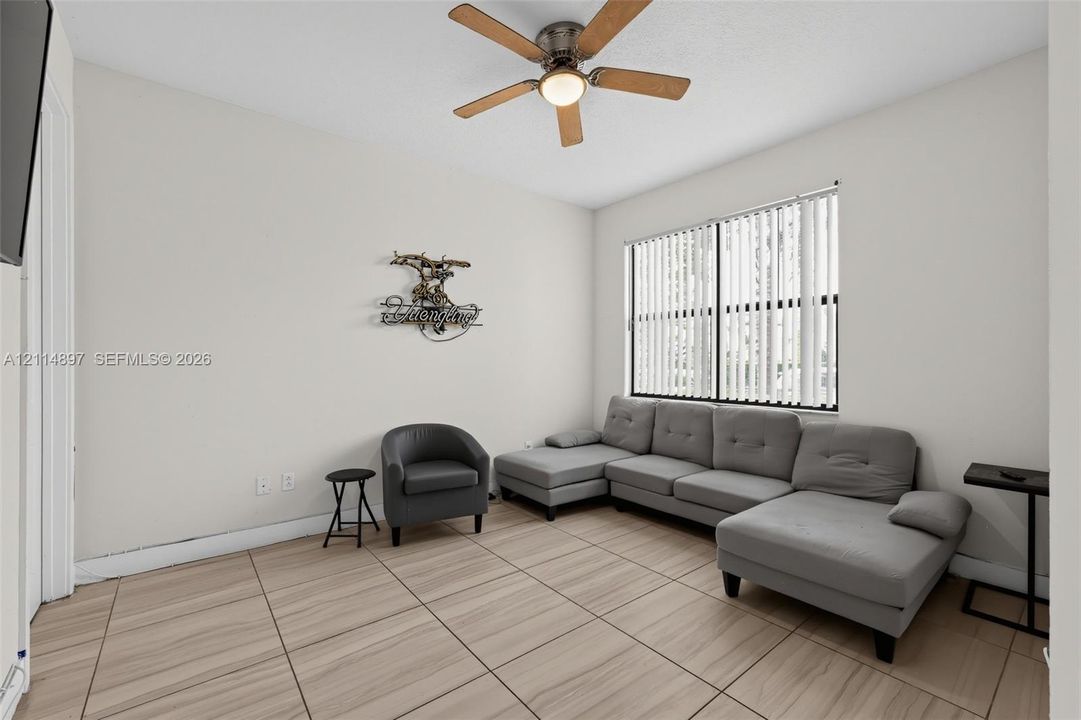 Interior space featuring wood-finish tile flooring, ceiling fan with integrated lighting, and vertical window blinds
