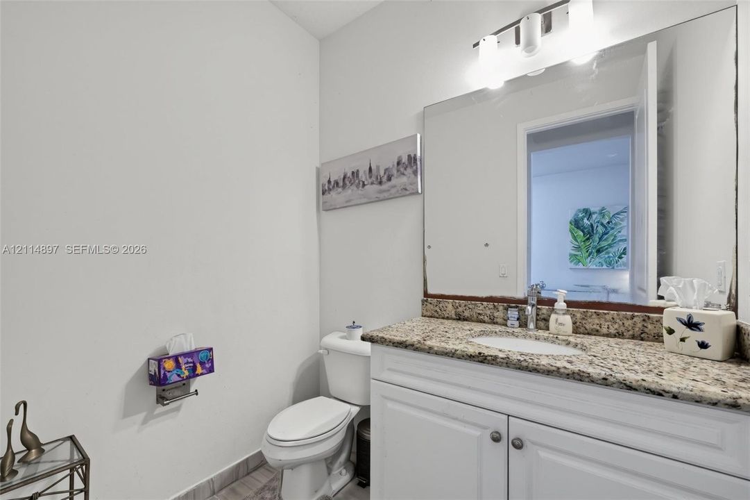 Bathroom featuring a white vanity cabinet, neutral stone-finish countertop with an integrated oval sink, full-width mirror, and three-bulb vanity light fixture