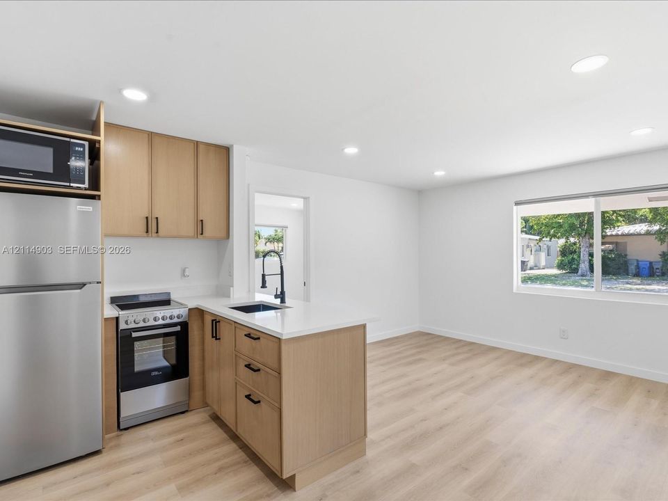 Kitchen featuring light-tone cabinetry, quartz countertops, stainless steel appliances, a matte black faucet, and wood-finish flooring