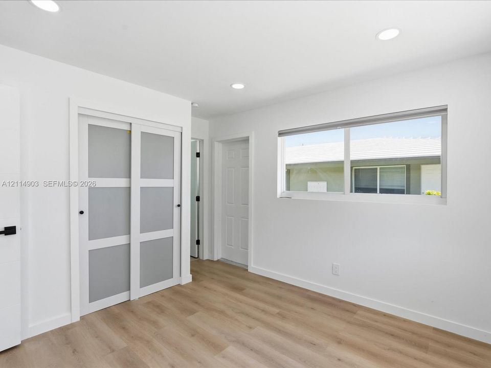 Interior room featuring wood-finish flooring, recessed lighting, sliding closet doors with frosted panels, and a multi-pane horizontal window