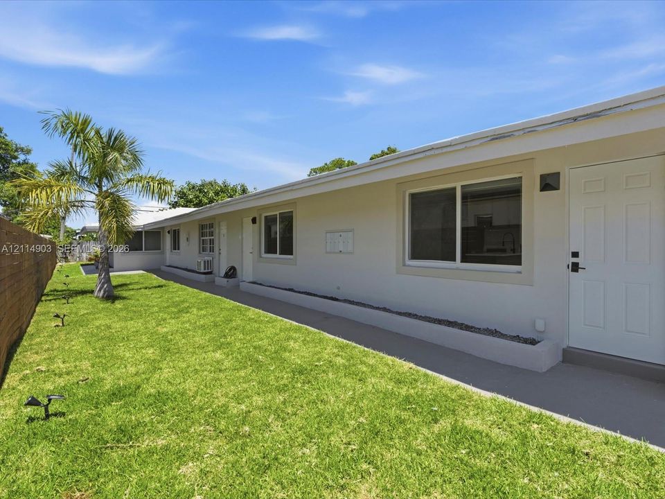 Exterior featuring a manicured lawn, palm tree, concrete pathway, and horizontal wood-slat fencing