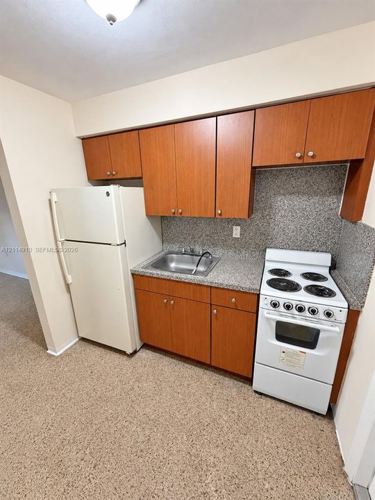 Kitchen featuring wood-finish cabinetry, stone-texture countertops, a stainless steel sink, and white appliances