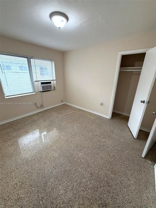 Room featuring polished aggregate flooring, neutral wall tones, a built-in closet with overhead shelving, and a dual-pane window