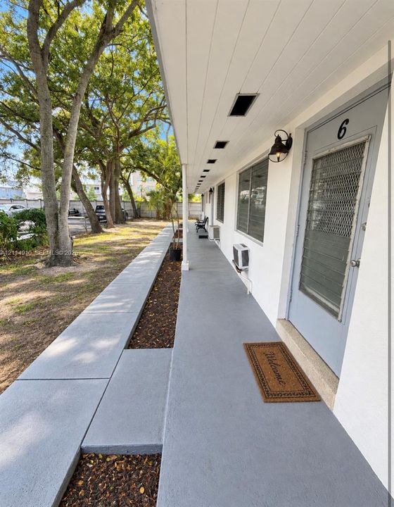 Covered walkway featuring a painted concrete surface, exterior wall-mounted lighting, recessed ceiling lighting, and a metal screen door