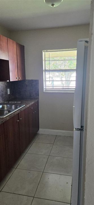 Kitchen featuring dark-toned cabinetry, a stainless steel sink, tile flooring, and a single-pane window
