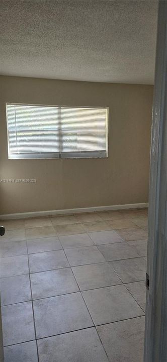 Neutral-toned interior space featuring light-colored square tile flooring, a horizontal slider window, and textured ceiling finish