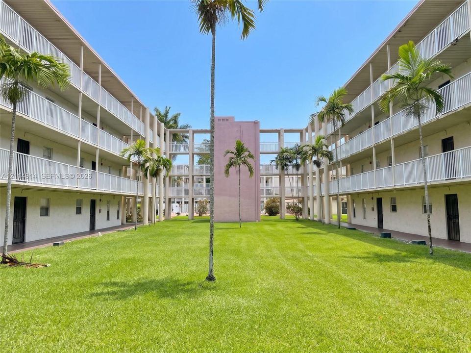 Central courtyard featuring a manicured lawn, perimeter palms, and tiered structural balconies with metal railings