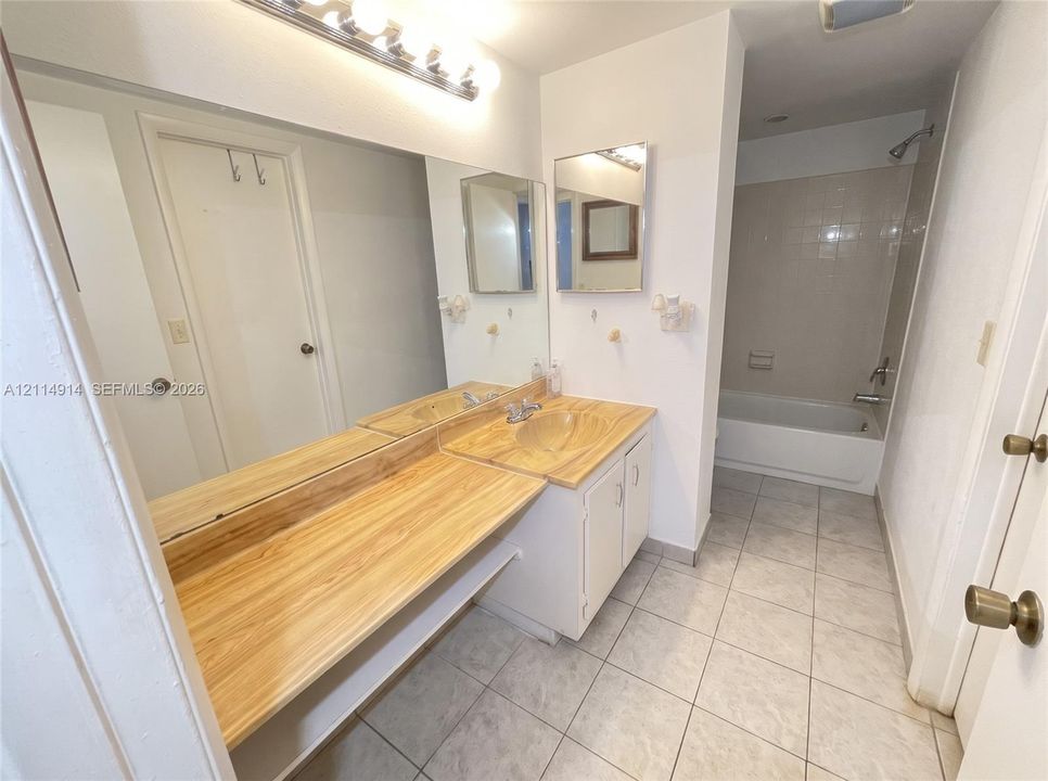 Bathroom featuring an extended vanity with wood-finish countertop, integrated sink, full-width vanity mirror, tile flooring, and a tub-shower combination