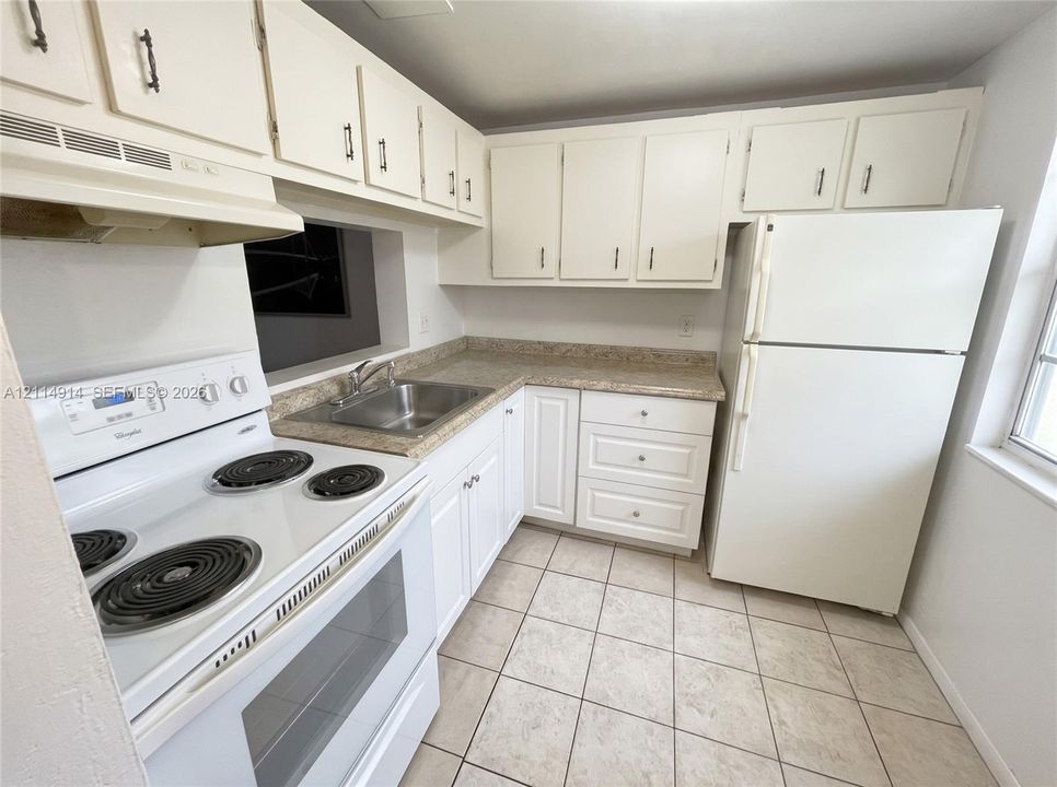 Kitchen featuring white cabinetry, solid-surface countertops, tile flooring, stainless steel drop-in sink, and integrated white appliances