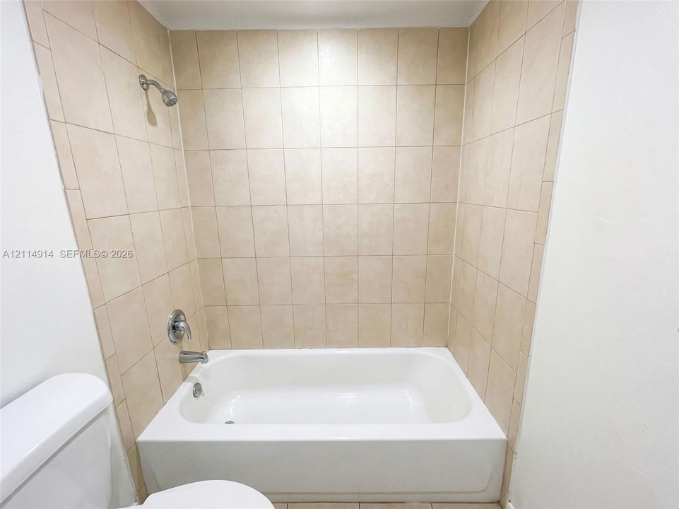 Bathtub with a white surround, neutral-toned square wall tile, and polished chrome shower fixture