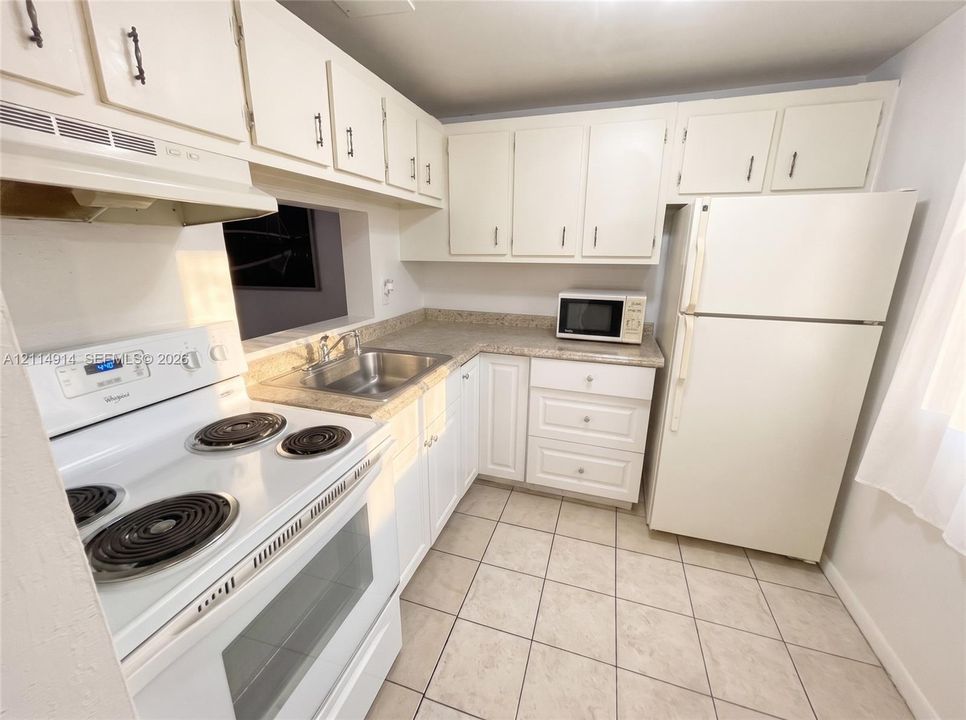 Kitchen featuring white shaker-style cabinetry, solid-surface countertops, a stainless steel dual-basin sink, and tile flooring