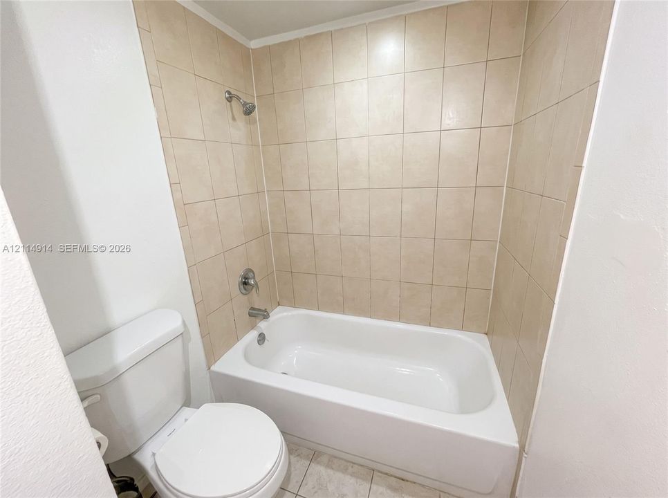 Bathtub with a shower head, tiled surround, and white porcelain toilet