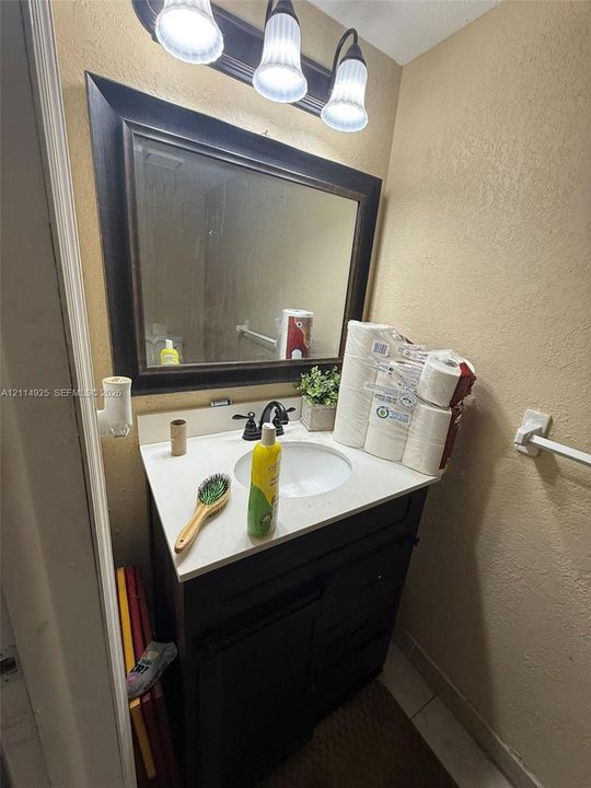 Dark wood-finish vanity with a white countertop and undermount sink, accompanied by a framed vanity mirror, three-light fixture, and matte black hardware