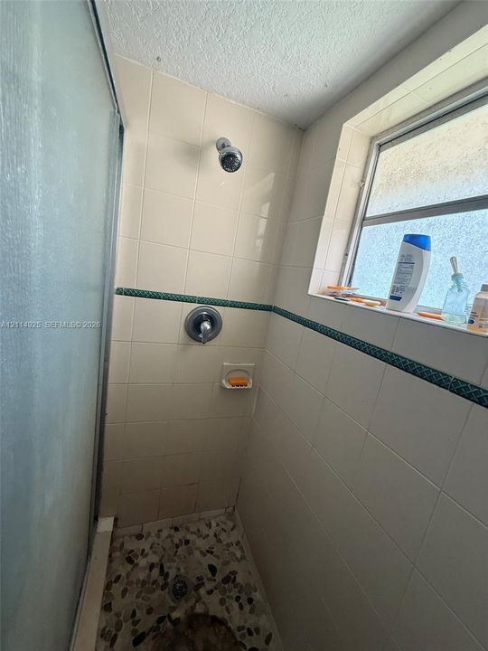Shower stall featuring white wall tile with decorative accent trim, a single-handle faucet, a built-in soap dish, a window, and pebble-style floor tiling
