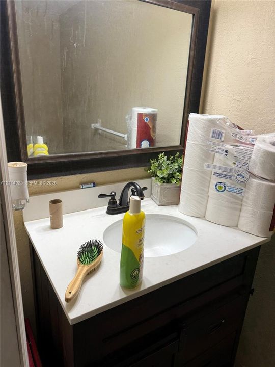 Bathroom vanity featuring a stone-composite countertop, undermount sink, dark wood-finish cabinetry, and oil-rubbed bronze faucet hardware, complemented by a framed mirror