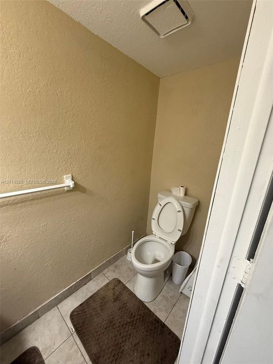 Restroom featuring a two-piece white porcelain toilet, light-toned ceramic tile flooring, and a wall-mounted metal towel bar