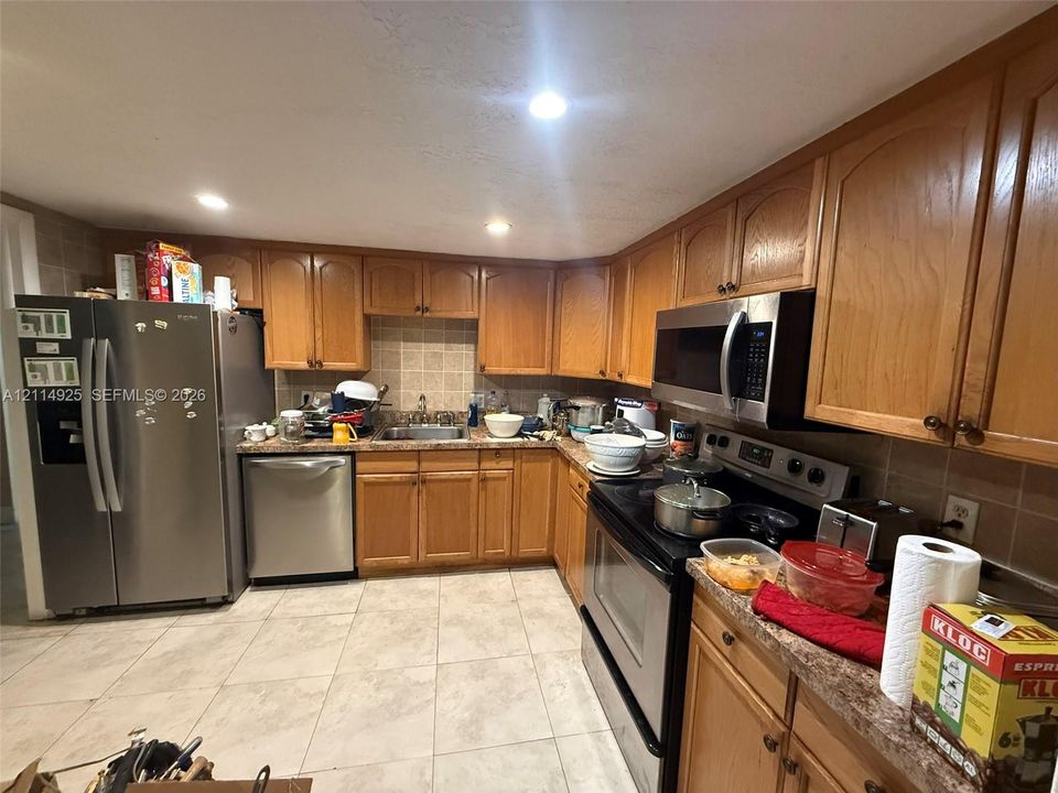 Kitchen featuring natural finish wood cabinetry, stainless steel appliances, neutral tile flooring, and tile backsplash