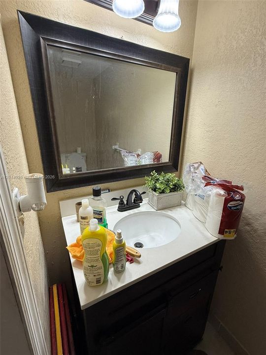 Vanity cabinet with a white countertop and integrated sink, complemented by a dark-toned framed mirror and a dual-handle faucet
