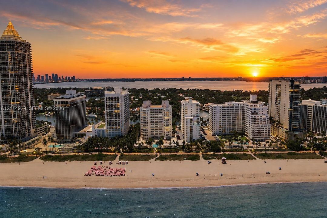 Aerial perspective of oceanfront high-rise residential buildings situated along a sandy beach shoreline with a sunset horizon backdrop