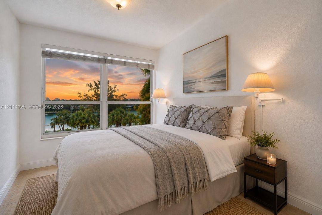 Oversized windows featuring water and sunset scenery, wall-mounted swing-arm lamps, and neutral-toned wall finishes