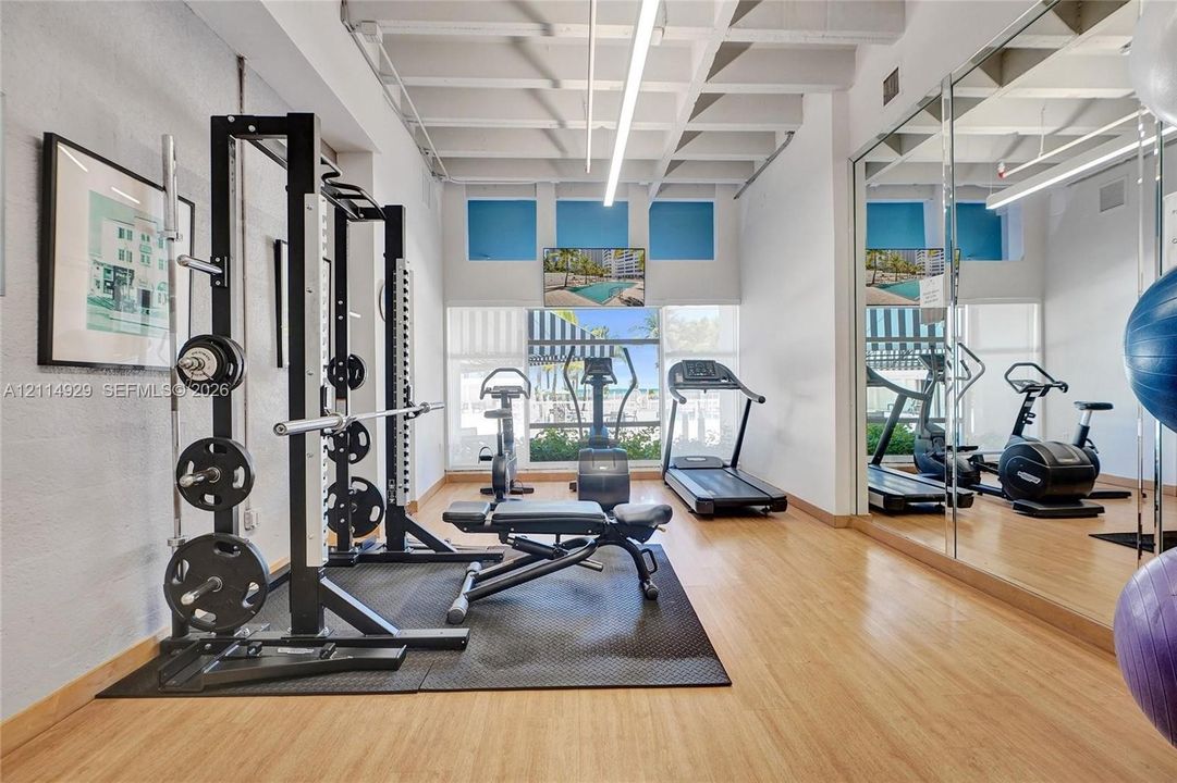 Fitness space featuring wood-finish flooring, exposed beam ceiling, mirrored wall, and overhead linear lighting