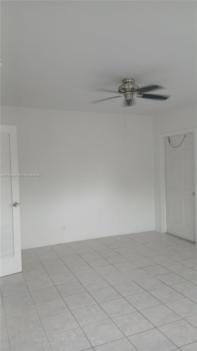 Interior room featuring neutral wall-to-wall ceramic tile flooring, a brushed-nickel ceiling fan, a louvered closet door, and a multi-panel door