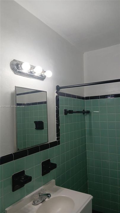 Wall-mounted three-bulb chrome light fixture, rectangular medicine cabinet, integrated sink vanity, and custom green wall tile with black trim accents
