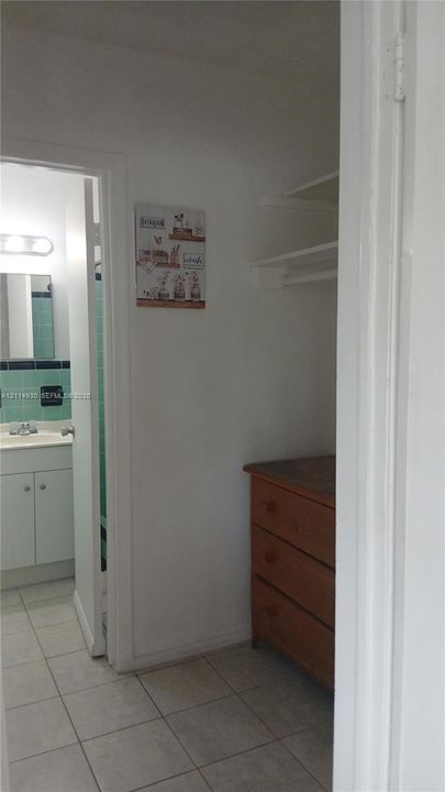 Walk-in closet with built-in shelving, tiled flooring, and a bathroom featuring a vanity with integrated sink and tile wall accents