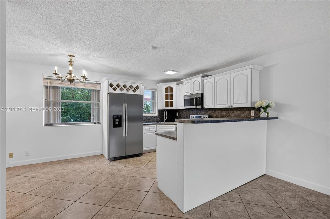 Kitchen featuring white shaker-style cabinetry, stainless steel appliances, a built-in wine rack, stone-finish countertops, and tile flooring