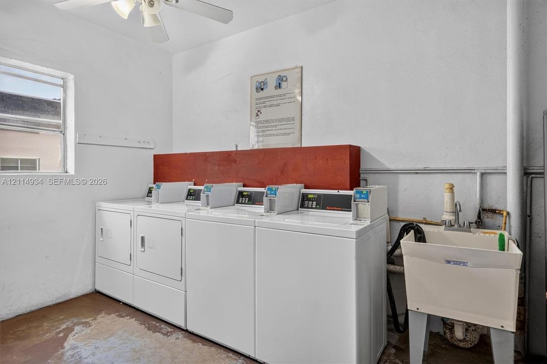 Laundry space featuring multiple coin-operated washing machines, a dedicated utility sink, and a ceiling-mounted fan