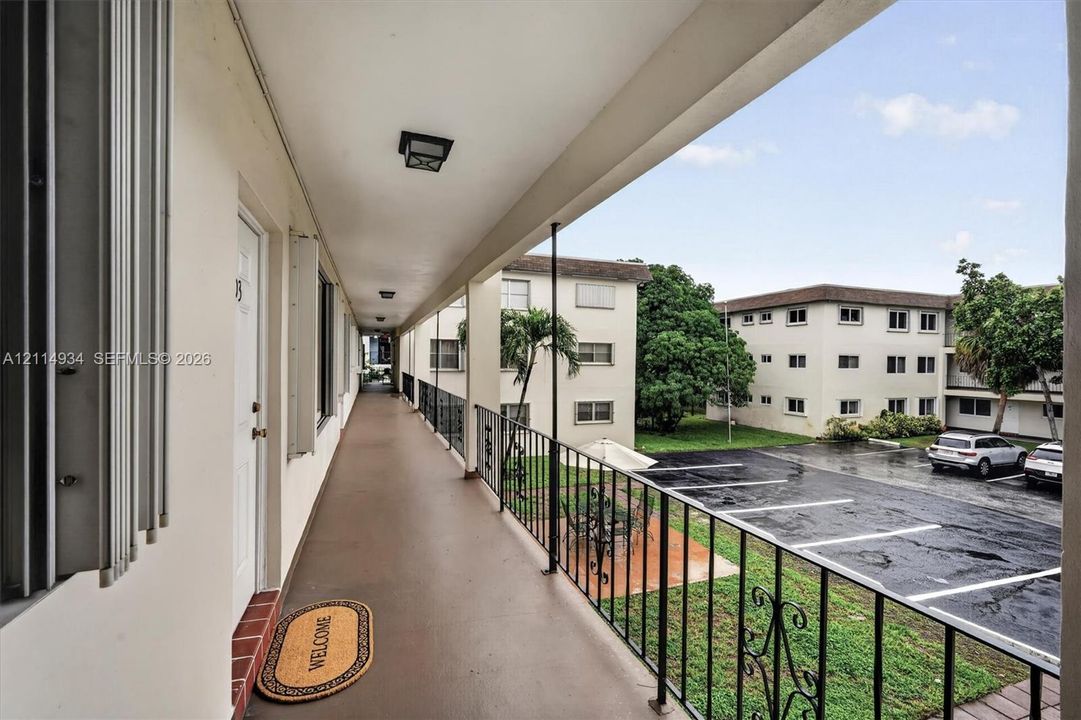 Covered exterior walkway featuring a smooth concrete surface, flush-mount ceiling lighting, and decorative black metal railings