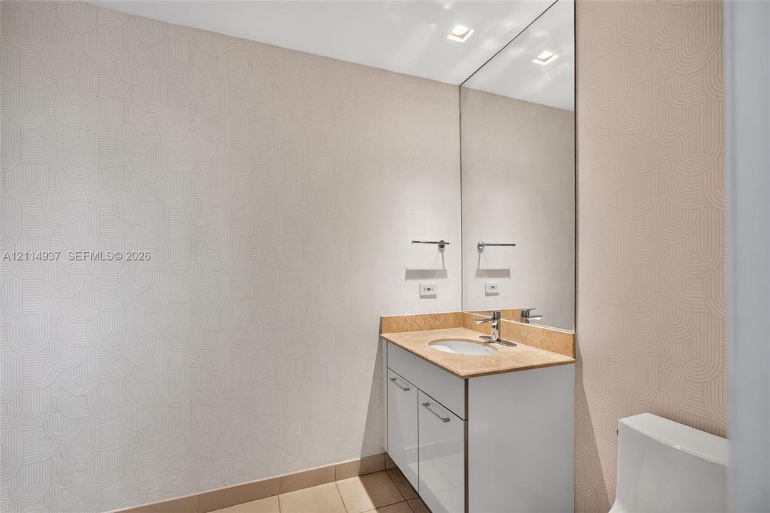 Wall-mounted vanity featuring a stone countertop, oval undermount sink, high-gloss cabinetry, floor-to-ceiling mirror, and textured wallpaper