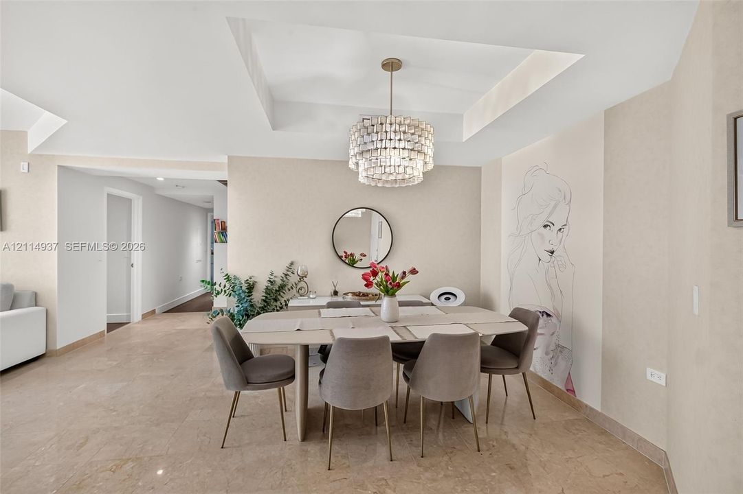 Tray ceiling featuring a multi-tiered crystal chandelier, polished stone flooring, and built-in wall mural