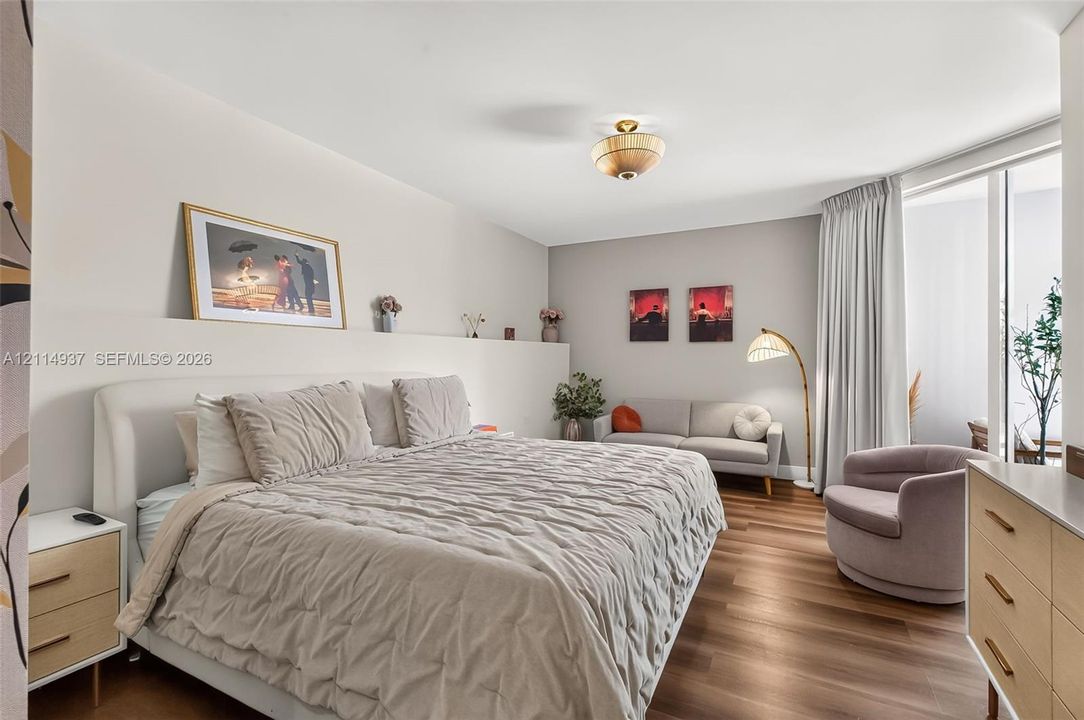 Wood-finish flooring, custom built-in headboard niche, flush-mount lighting, and expansive floor-to-ceiling glass panel door