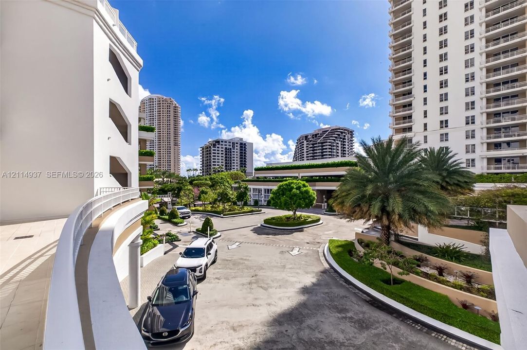 Paved motor court featuring a central landscaped island, manicured hedges, and mature palm trees