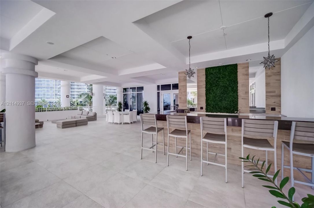 Covered outdoor lounge featuring large-format tile flooring, a built-in bar with wood-finish cladding, structural columns, and star-shaped pendant lighting