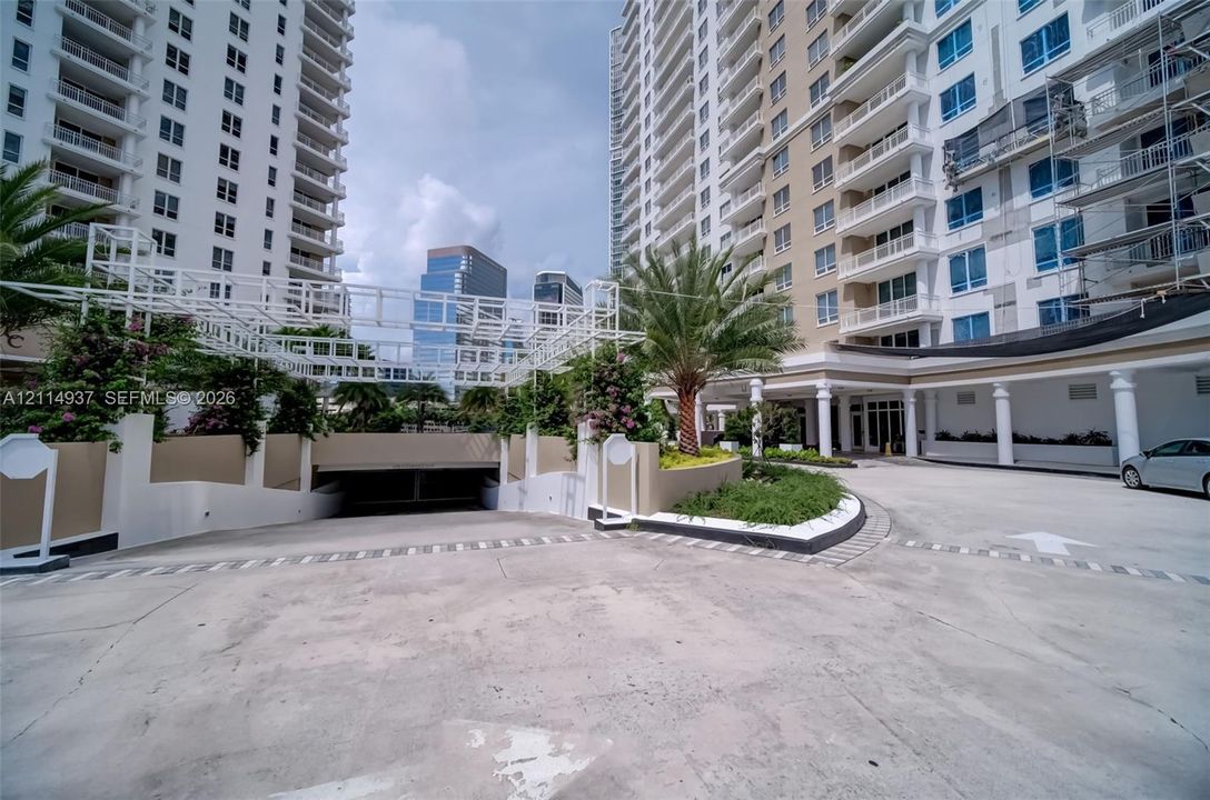 Entrance area featuring a covered drive, subterranean parking garage, concrete hardscaping, manicured landscaping, and structural columns