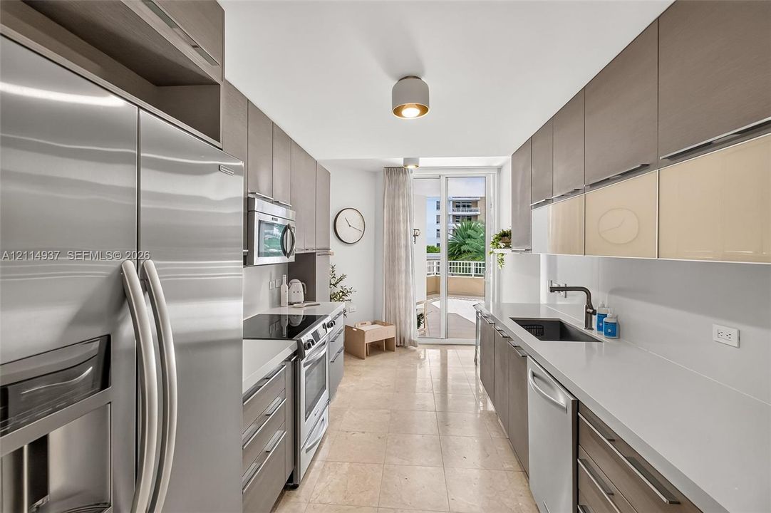 Galley kitchen featuring flat-panel cabinetry, stone countertops, stainless steel appliances, a deep undermount sink with a gooseneck faucet, and stone flooring